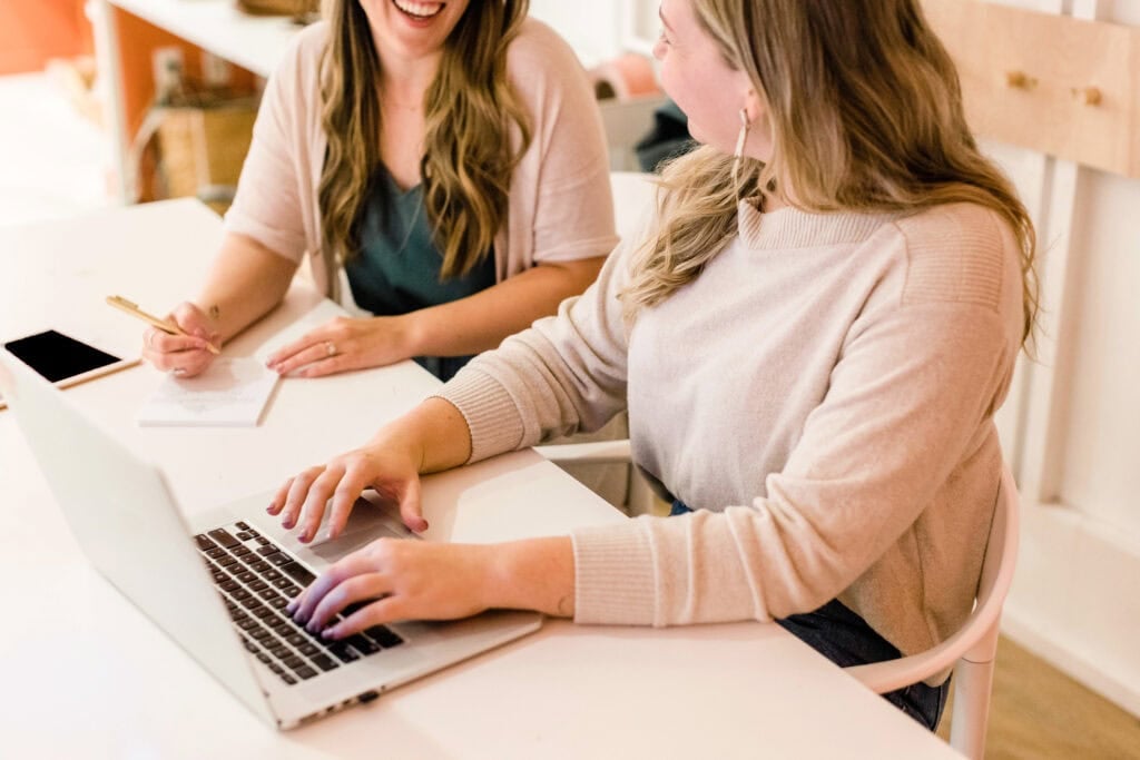 Two people sitting next to each other talking at a desk for an article about how to make $6,000 a month